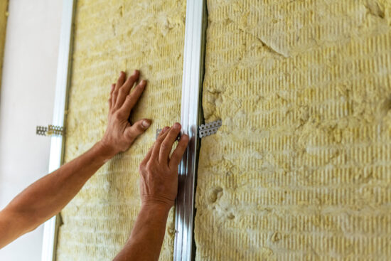 Artisan isolant le mur d'une pièce avec de la laine de roche minérale.