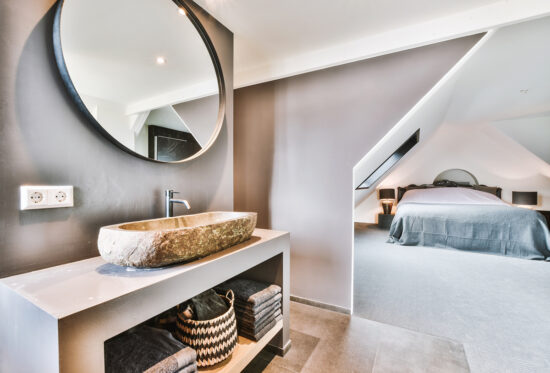 Salle de bains élégante avec lavabo en pierre et chambre ouverte à l'étage mansardé d'un appartement moderne.