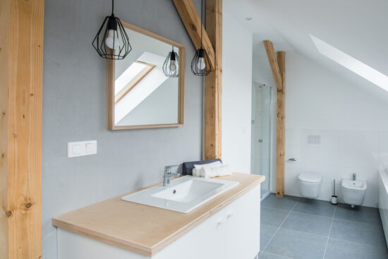 Salle de bains moderne et lumineuse avec murs gris, miroir et baignoire.